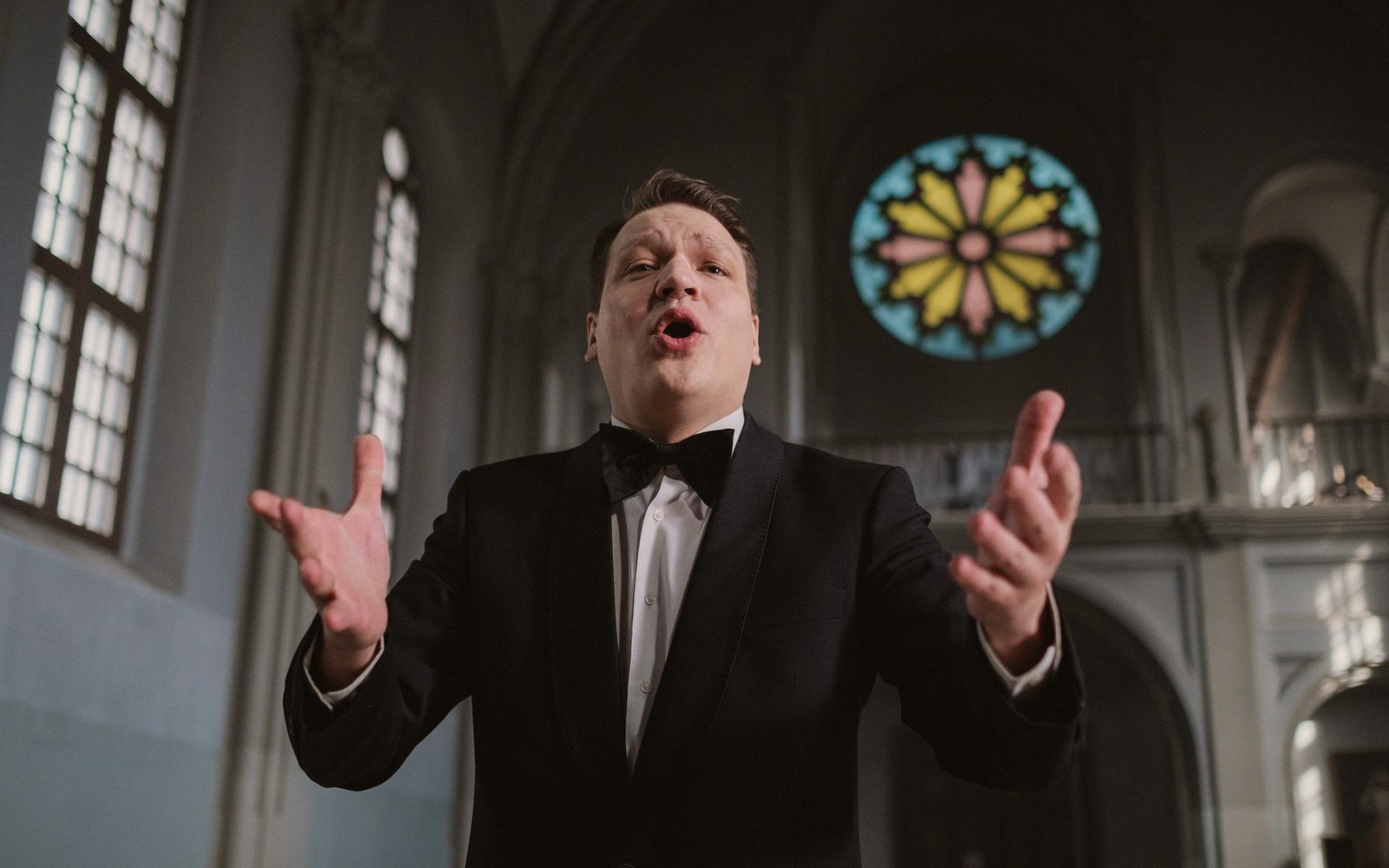 A singer performing, arms open, in a stone interior