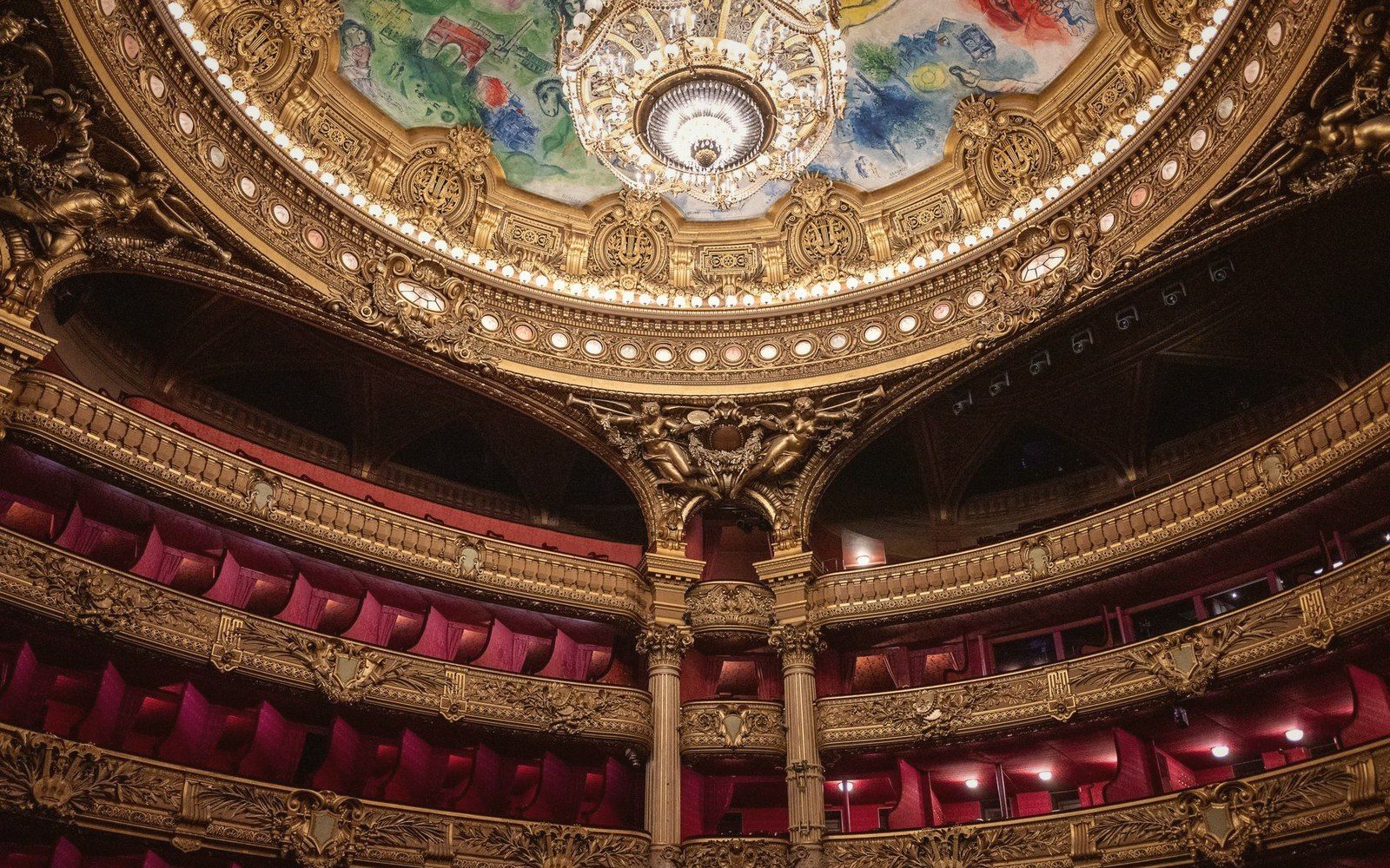 Ornate gilded opera house interior with painted domed ceiling and tiered red velvet balconies