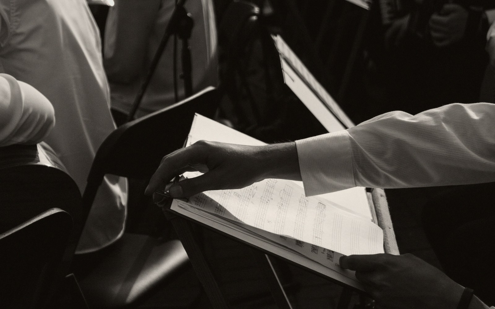 A full orchestral score open on a conductor's stand, pencil annotations visible in the margins, pit lighting from below